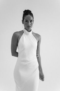 a black and white photo of a woman wearing a dress with high neck, standing in front of a plain background