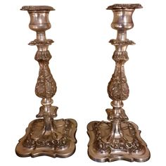 two silver candlesticks are sitting side by side on a white background, one has an ornate design