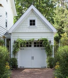 a white house with two garage doors and some plants on the side of the building