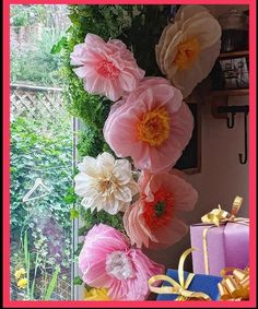 pink and yellow paper flowers are hanging from a window sill in front of presents