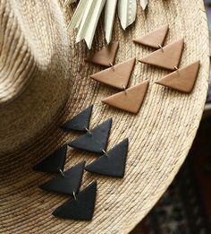 four triangle shaped leather earrings sitting on top of a straw hat next to other items