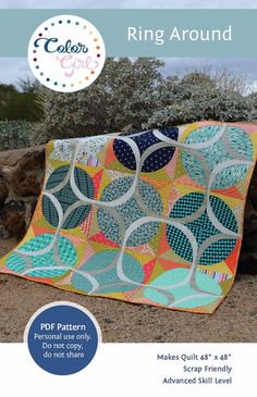 a patchwork quilt sitting on top of a rock wall next to some plants and bushes