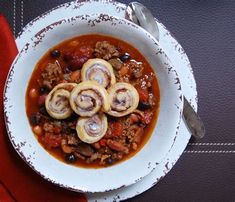 a white bowl filled with food on top of a red cloth covered place mat next to a silver spoon