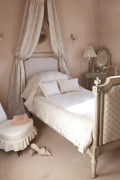 a white bed sitting in a bedroom next to a chair and window with drapes