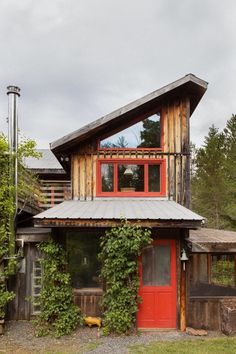 a red door and window in front of a wooden building with ivy growing on it