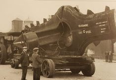 two men standing next to a large truck with a huge object on it's back