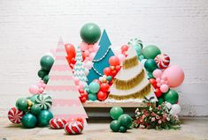 an assortment of christmas decorations and balloons in front of a white brick wall with a tree