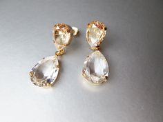 "These beautiful elegant earrings are made with fancy transparent teardrop shape Swarovski crystals hanging from the champagne colored studs. Available in gold, rose gold or silver finish. Available in champagne, dusty blue or clear crystal option. Shown in the video in champagne option. - 1 1/2\" long in total length and 1/2\" wide" Gold Pear-shaped Teardrop Earrings For Wedding, Gold Teardrop Wedding Earrings, Pear-shaped Teardrop Earrings For Party, Gold Pear-shaped Teardrop Earrings For Party, Gold Teardrop Earrings For Bridesmaid Gift, Gold Pear-shaped Bridal Earrings For Party, Crystals Hanging, Teardrop Bridal Earrings, Crystal Hanging