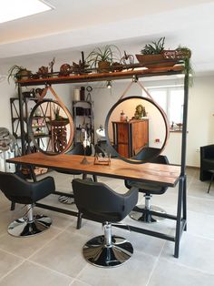 a salon table with chairs and mirrors in the middle of an open room, surrounded by potted plants