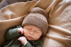 a newborn baby wearing a brown knitted hat and green sweater sleeping on a blanket