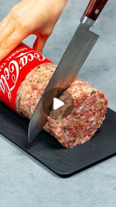 a person cutting meat with a large knife on top of a black board next to a can of coca - cola