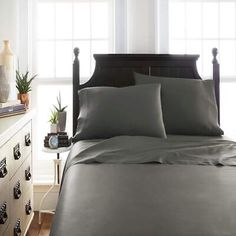 a bed with grey sheets and pillows in a bedroom next to a window, near an end table