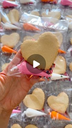 a person holding up a heart shaped cookie in front of some other cookies on plastic wrappers