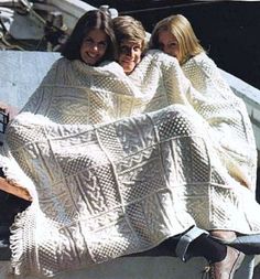 three women wrapped up in blankets sitting on a bench