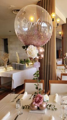 a table with white and pink flowers on it in front of a large balloon that says happy