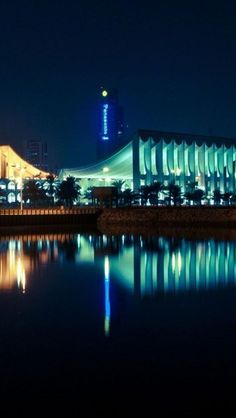 a large building sitting next to a body of water in front of a city at night