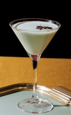 a martini glass filled with white liquid on top of a wooden table next to a silver tray