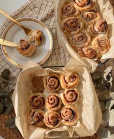 two trays filled with cinnamon rolls on top of a table next to a plate