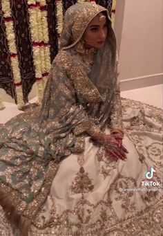 a woman sitting on top of a bed wearing a white and blue wedding dress with gold accents