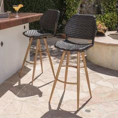 two black wicker bar stools sitting next to an outdoor kitchen counter with drinks on it