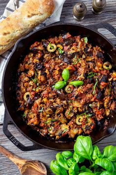 a skillet filled with meat and vegetables on top of a table next to bread