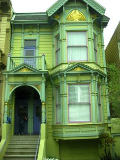 a green two story house with yellow trim and sunbursts on the windows