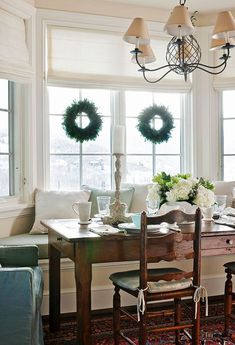 a dining room table and chairs with wreaths on the windowsill