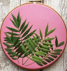 a close up of a embroidery on a wooden surface with green leaves and pink background