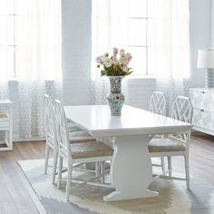 a white dining room table with chairs and a vase filled with flowers on top of it