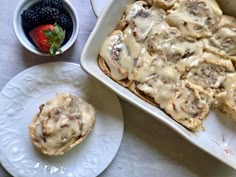 a pan filled with cinnamon rolls next to a bowl of berries and a cup of coffee