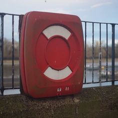 a red box sitting on the side of a fence next to a body of water