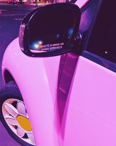 a pink car parked in front of a building with its side mirror on it's side