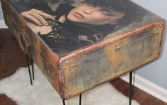 an old suitcase is sitting on the floor in front of a wall with a woman's face painted on it