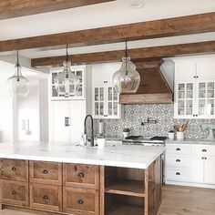 a large kitchen with white cabinets and wooden beams on the ceiling, along with marble counter tops