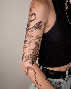 a woman with a snake and flowers tattoo on her arm is standing in front of a wall