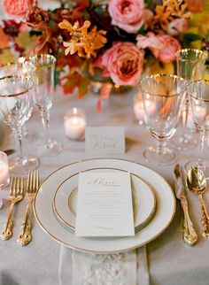 an elegant table setting with gold and white plates, silverware, and pink flowers