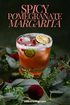 a cocktail with pomegranate and lime garnish on the rim, surrounded by greenery