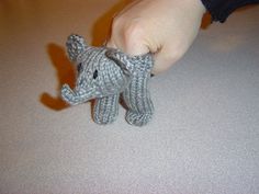 a small gray knitted elephant is being held by someone's hand on the floor