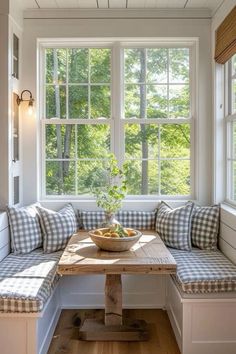 a wooden table sitting under a window next to a bench with pillows on top of it