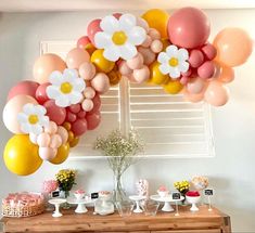 a table topped with lots of balloons and flowers on top of it next to a window