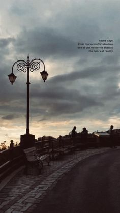 people are sitting on benches near a street light and lamp post with the sky in the background