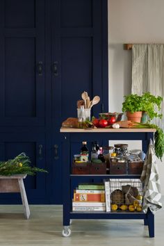 a kitchen with blue painted cabinets and wooden floors, including an island cart filled with food