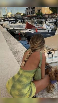 a woman sitting on the dock with her dog next to some boats and buildings in the background