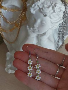 a hand holding three small white and yellow flowers on it's earwires