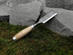 a large knife laying on top of a green moss covered ground next to a rock