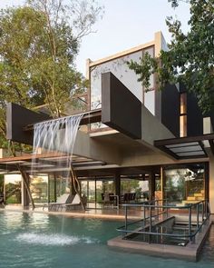 a modern house with a pool and waterfall in the front yard, surrounded by trees