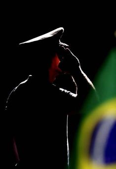 a man wearing a hat standing in front of a green and yellow flag with his hands to his face