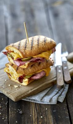 a sandwich with meat and cheese is on a cutting board next to some knifes