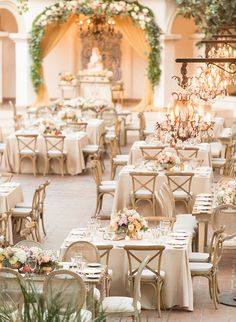 tables and chairs are set up in an outdoor setting with chandeliers hanging from the ceiling