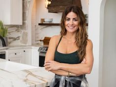 a woman standing in a kitchen with her arms crossed and looking at the camera smiling